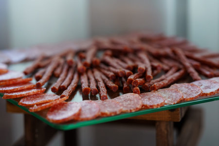 A beautifully arranged display of sliced salami and stick-style salami on a glass serving tray,...