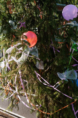 Colorful balloons and purple ribbons decorate a dense evergreen tree in a cheerful holiday scene...
