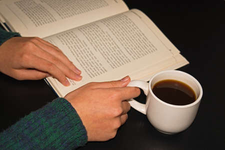 Girl reads a book with cup of hot coffe on black background. Ideas Conceptの写真素材