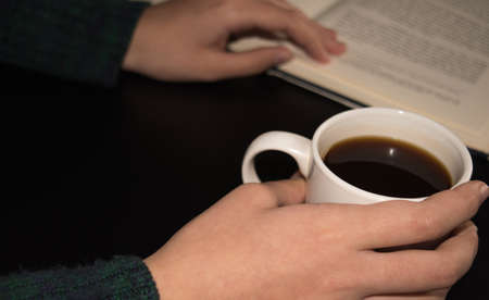 Girl reads a book with cup of hot coffe on black background. Ideas Conceptの写真素材
