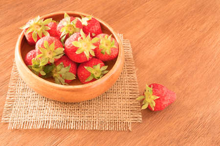 Ripe red strawberries in bowl on wooden table, close upの写真素材