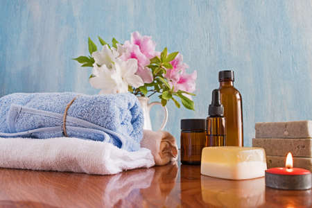 Spa and wellness setting with natural soap and flowers, candles, massage oils and soft blue towel.の写真素材