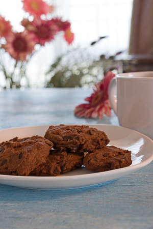 chocolate chip cookies on white plate wih cup of coffe on blue background