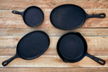 Set of four round and oval cast iron skillets of different sizes on a wooden background. Viewed from above on a rustic wooden table background. Kitchen equipment.の写真素材