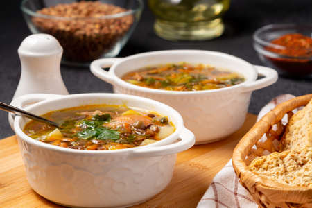 Lentil soup with chicken in a two white bowls on a wooden board on a black table and ingredientsの写真素材
