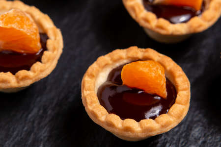 Sweet tartlets with chocolate and slices of tangerine on a dish of natural slate for serving, close-upの写真素材