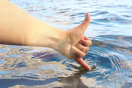 Female hand touches the water with a finger and shows that it is warm and clean. Summer vacation and swimming conceptの写真素材