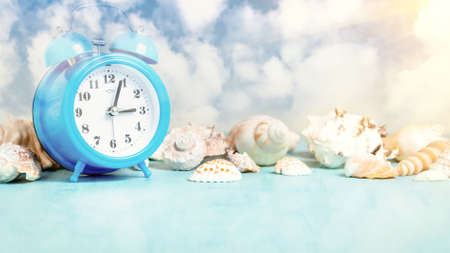 Seashell border and an alarm clock on a blue table against a blue sky with clouds - summer holidays...