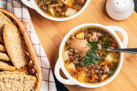 Two plates with lentil soup and chicken on a wooden board on black table, top viewの写真素材