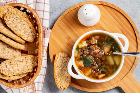 Lentil soup with chicken in a white bowl on a wooden board on a gray table, top viewの写真素材