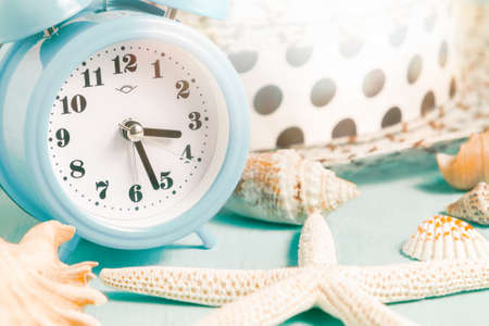 Seashells, alarm clock and beach accessories on a blue table - summer vacation and vacation time...