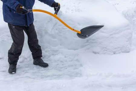 A man cleans snow in the yard with a shovel after a heavy snowfallの写真素材