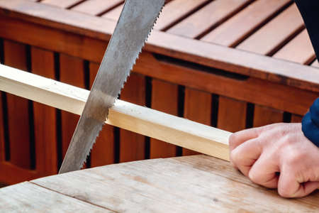 Mens hands sawing a wooden bar with a hacksawの写真素材