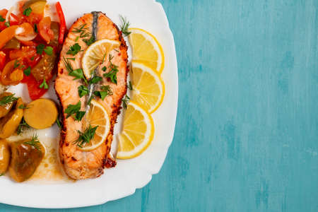 Baked salmon fillet medallion with salad of pickled vegetables and mushrooms on a white plate on a blue background, top view, flatlay, place for text, copy spaceの写真素材