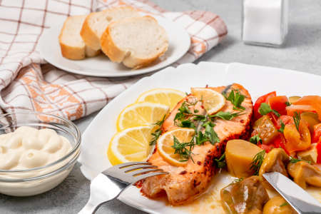 Baked salmon fillet medallion with salad of pickled vegetables and mushrooms on a white plate on a gray backgroundの写真素材