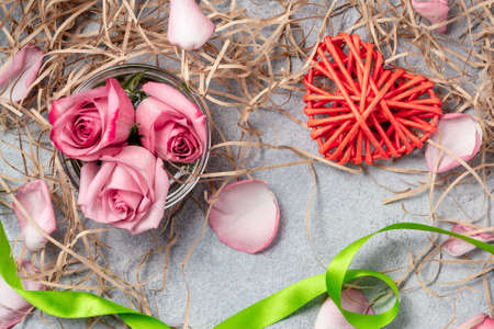 pink roses and a wicker heart with decorations on the table-a concept of love and congratulations for a loved oneの写真素材