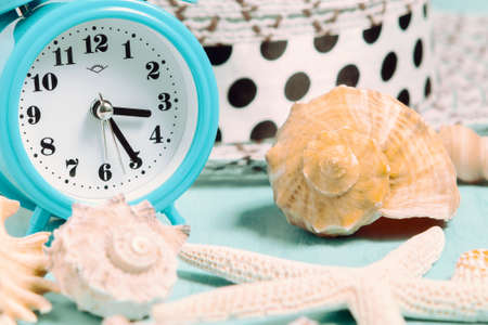 Seashells, alarm clock and beach accessories on a blue table - summer vacation and vacation time conceptの写真素材