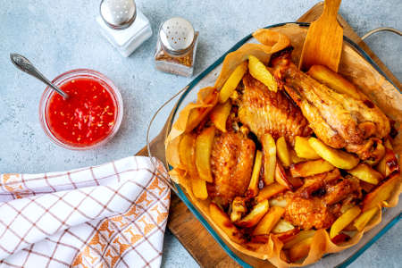 Baked turkey wings with potato pieces in a square baking dish on a gray kitchen table with sauce and...