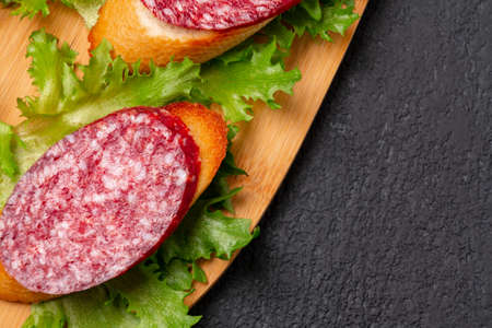 Several sandwiches with sausage and salami and sauce on a black board, background with copyspace
