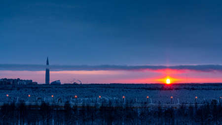 Colorful sunset in the cloudy sky over a snowy forest on the outskirts of the cityの写真素材