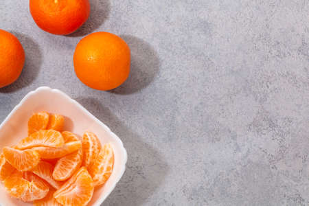Several whole and peeled ripe tangerines on a white plate on gray background with space for text, flat lay, top viewの写真素材