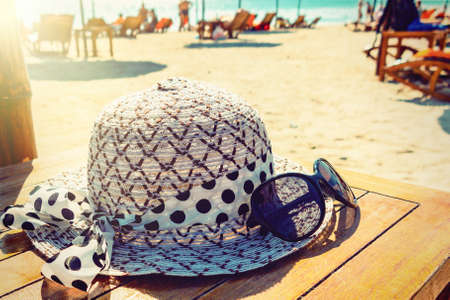 Womens hat and sunglasses lie on a wooden table on a sunny sandy beach by the seaの写真素材