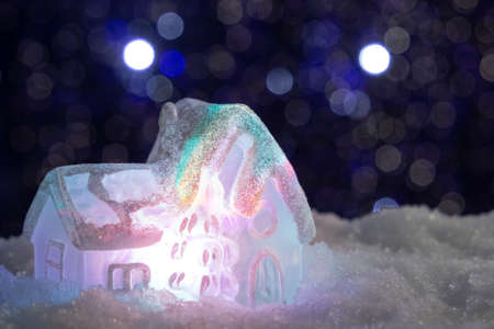 Glowing toy house in the snow on the background of Christmas lights. Festive, Christmas or New Year conceptの写真素材