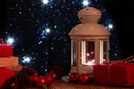 White lantern with a burning candle and boxes with gifts on the background of the Christmas tree...