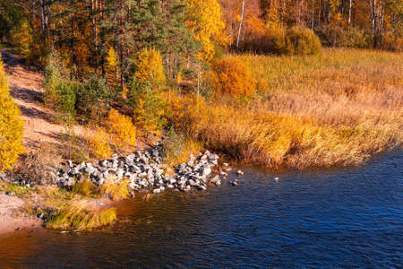 Bank of the river with stones on the edge of a sunny autumn day
