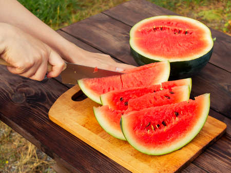 Womens hands cut with a knife into slices of ripe watermelon on a wooden tableの写真素材