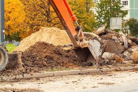 Road repair on a city street, an excavator bucket rakes in the ground, close-up