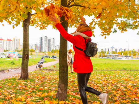 SAINT-PETERSBURG, RUSSIA - OCTOBER 8, 2018: Young beautiful girl blonde in a red jacket and her boyfriend enjoying a warm autumn day in the park and having fun playing with autumn maple leavesのeditorial素材