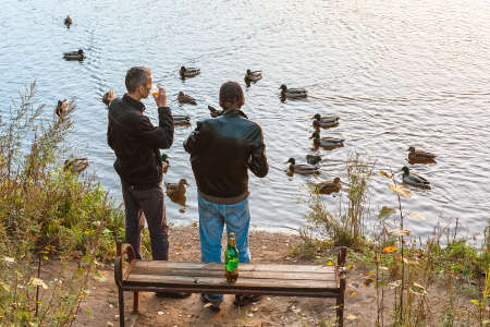 SAINT-PETERSBURG, RUSSIA - OCTOBER 8, 2018: Two men drink beer on the river bank and watch the ducks at sunset.のeditorial素材