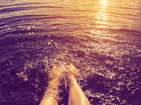 Womens feet splashed sea water at sunsetの写真素材