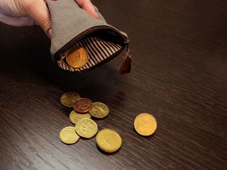 Several coins fall from an empty purse in a womans hand