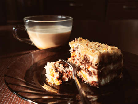 Piece of chocolate cake on a plate and a cup of coffee with milk on a dark wooden table in the kitchenの写真素材