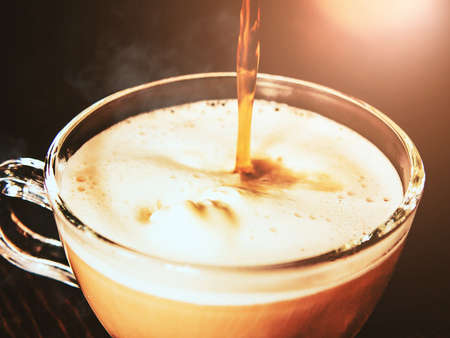 Hot coffee is poured from the turkish coffee makere into a transparent cup of ice cream