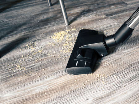 Garbage on the floor is cleaned with a vacuum cleaner. In the frame, a brush from a vacuum cleaner, legs of tables and chairs, a floor with a pattern for woodの写真素材