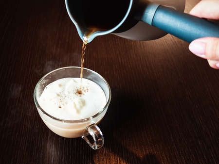 Hot coffee is poured from the turkish coffee makere into a transparent cup of ice cream