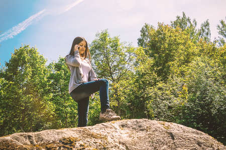 Young pretty girl smiles and talks on the phone while standing on a large stoneの写真素材