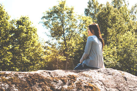 Young pretty girl sits on a big rock and admires natureの写真素材