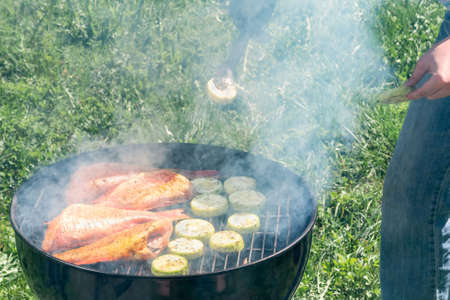 Picnic outdoors in the summer. Cooking on a round grill fish sea bass and zucchini slicesの写真素材