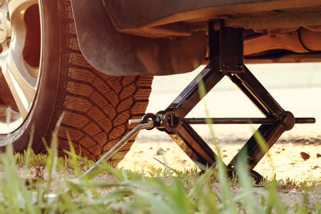 Replacing the wheels on the highway, the car is jacked, unscrewing the nuts with a tire ironの写真素材