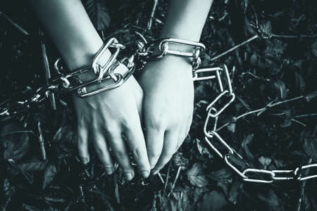 Womens hands chained in a dark forest - the concept of violence, hostage, slaveryの写真素材