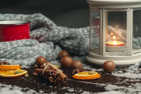 Lantern with a burning candle, spices and a red mug with hot coffee on a snowy wooden tableの写真素材