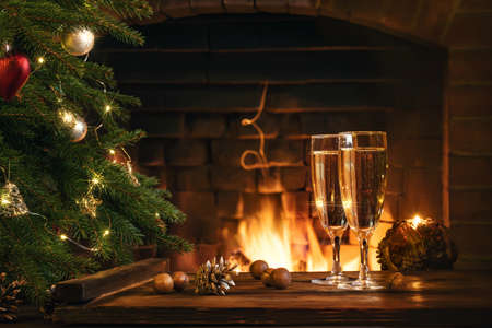 Christmas composition - Two glasses with champagne on a wooden table near a Christmas tree in a room with a burning fireplaceの写真素材