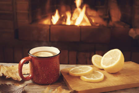 Red mug with hot tea with lemon in front of a burning fireplace, comfort and warmth of the hearth...