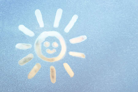 Smiling sun painted on a frozen window, winter fun, season change and hope conceptの写真素材