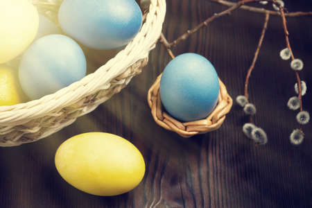 Easter composition - several colored eggs in a basket and on a dark wooden table with willow twigs