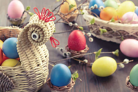 Easter composition - a wicker basket in the form of a chicken with colored eggs on a dark wooden...